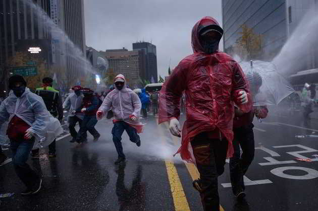 Anti-government protesters run between water cannons towards riot police in Seoul on November 14, 2015. Tens of thousands of people took to the streets in central Seoul in a massive protest against the conservative government's drive for labour reform and state-issued history textbooks. AFP PHOTO / Ed Jones        (Photo credit should read ED JONES/AFP/Getty Images)