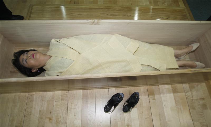 A woman, donning a traditional yellow hemp robe, lies down in a coffin during a "well-dying? course, run by a local district office in Seoul July 4, 2011. The course, run by a local district office in the northeast of Seoul, has an aim: "Don't take life for granted." While some see the mock funeral as a way to reflect on one's life and prepare for death, many sceptics still question whether death simulation can prevent suicide and blame some entrepreneurs for using this as a commercial event. Picture taken July 4, 2011. To match Reuters Life! KOREA-FUNERAL/ REUTERS/Truth Leem (SOUTH KOREA - Tags: ODDLY SOCIETY)